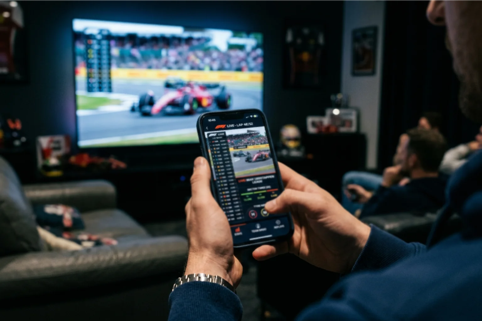 Mains tenant un smartphone avec contenu sportif en direct et télévision montrant une course F1 en arrière-plan